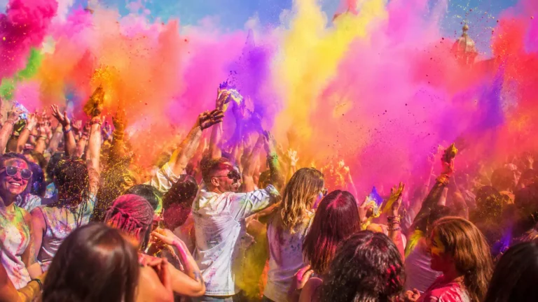 Une foule enthousiaste participe à un événement festif immersif, entourée de nuages de poudres multicolores éclatantes. Les couleurs vives rose, jaune, orange, violet et bleu remplissent l’air dans une ambiance dynamique et énergique, illustrant la viralité, l’engagement communautaire et l’impact des tendances sociales modernes.